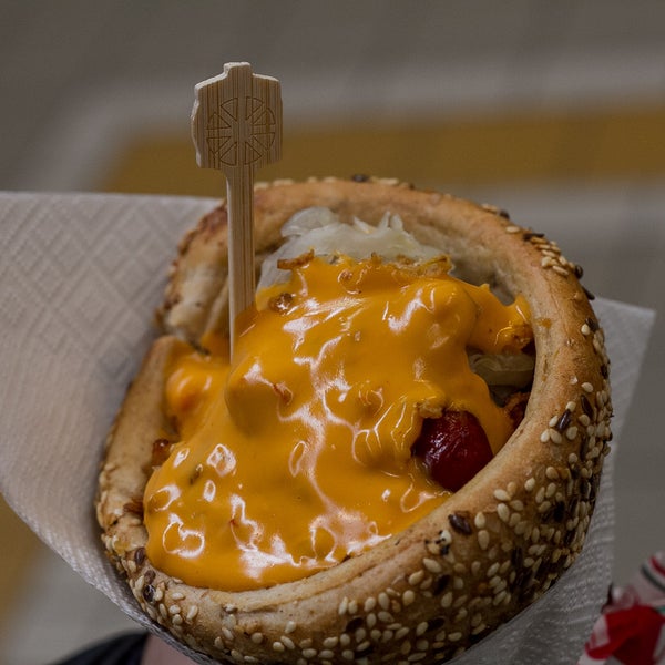 Being a street food place that sells sausages, we might ask: “How is it possible to eat a saucy sausage on the go in a civilized manner?” The answer hides in the seed-bread cone!