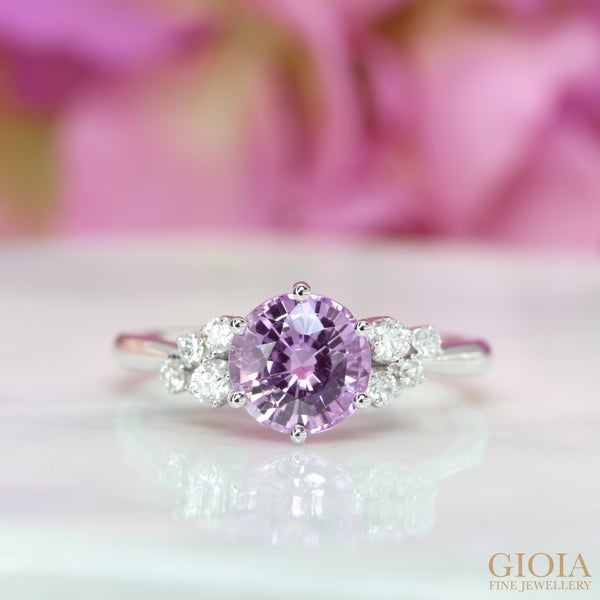 Violet Pink Sapphire Cluster Diamond Ring Featuring a unique round brilliant violet pink sapphire, designed with side diamonds encrusted together to form this beautiful engagement ring.