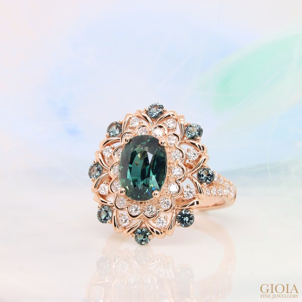 Art Deco Teal Sapphire Ring This stunning ring features a magnificent teal sapphire at its center, surrounded by a vintage-inspired diamond deco that beautifully complements the gem colour.