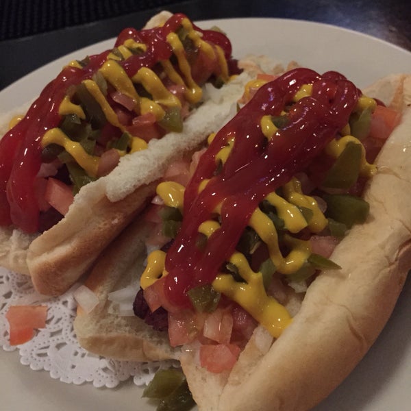 mexico city hochos - two bacon wrapped hot dogs topped with tomato, onion, pickled jalapeño, chipotle mayo, ketchup, and mustard