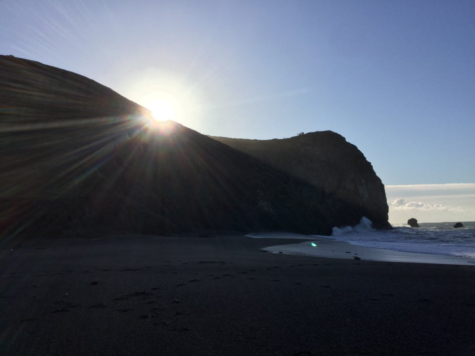 The sun rising over a hill just to the south of Tennessee Valley beach, sunbeams illuminating the surf, with most of the beach on the shadow of the hill.