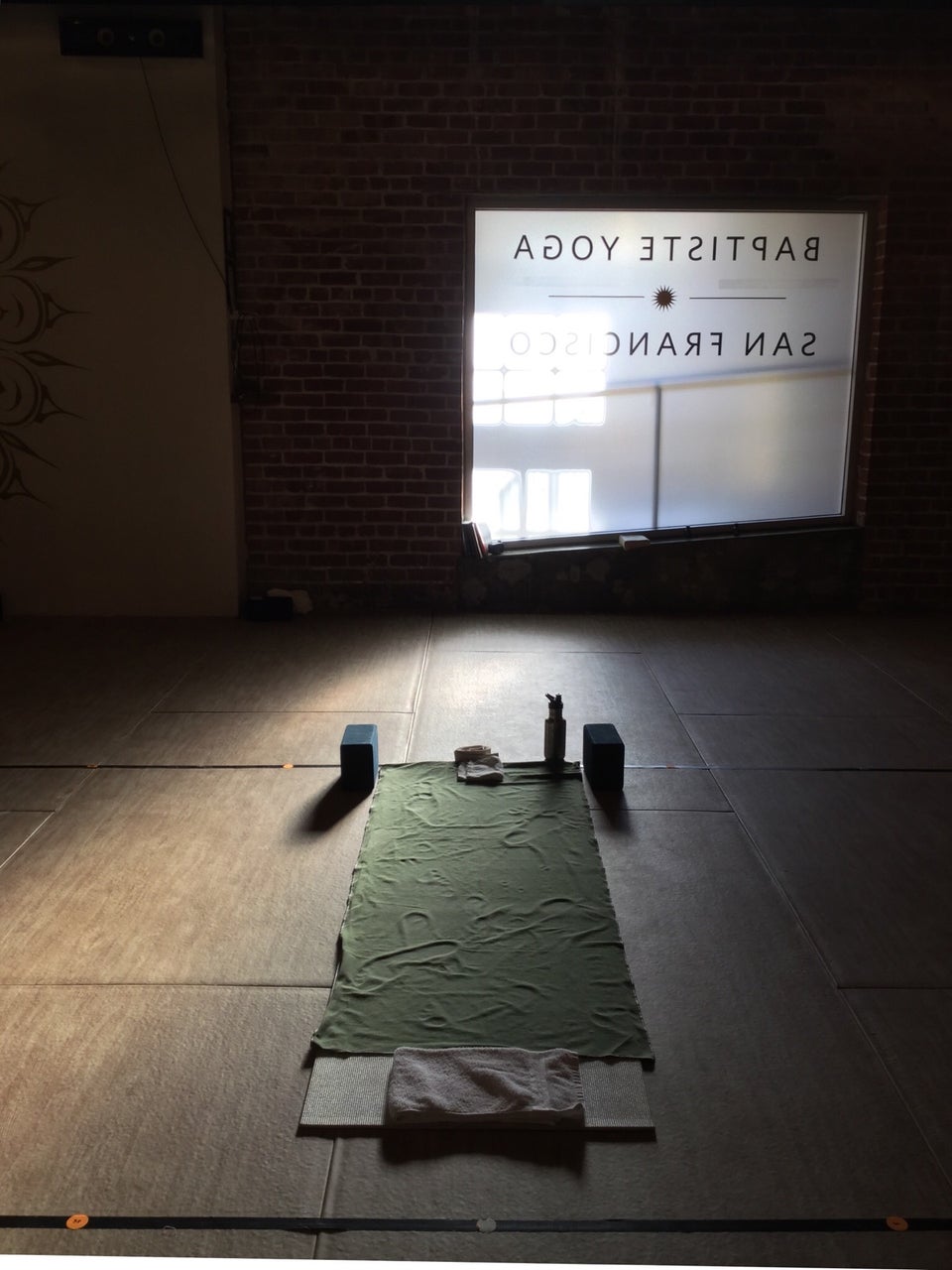 Inside the yoga room at Baptiste Yoga San Francisco, light coming in from the one window, lighting up a single yoga mat, blocks, towels, and water bottle.