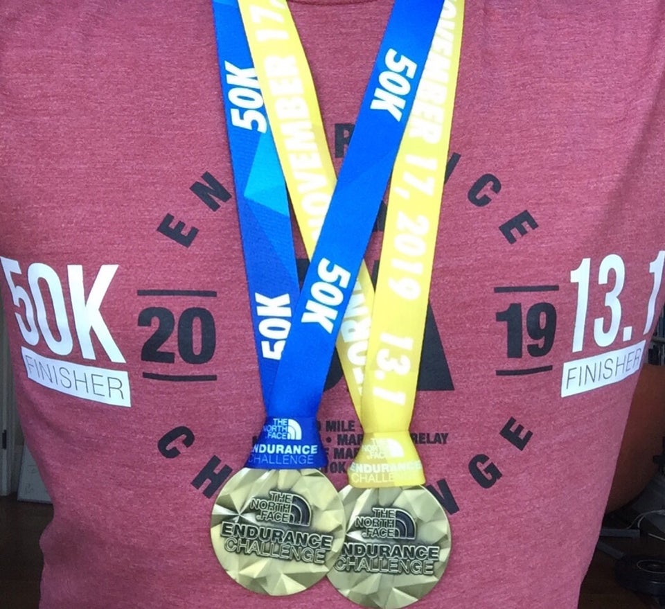 Wearing The North Face Endurance Challenge 2019 t-shirt with both 50k Finisher and 13.1 Finisher heat decals added, and 50k with blue ribbon and 13.1 Half Marathon with yellow ribbon medals hanging from the neck.