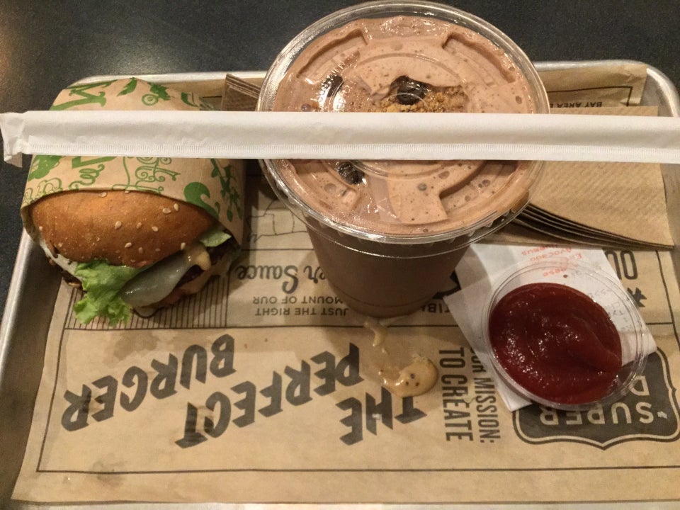 veggie burger, chocolate milkshake with an unopened straw on top, and a small container of kethcup on a tray with napkins