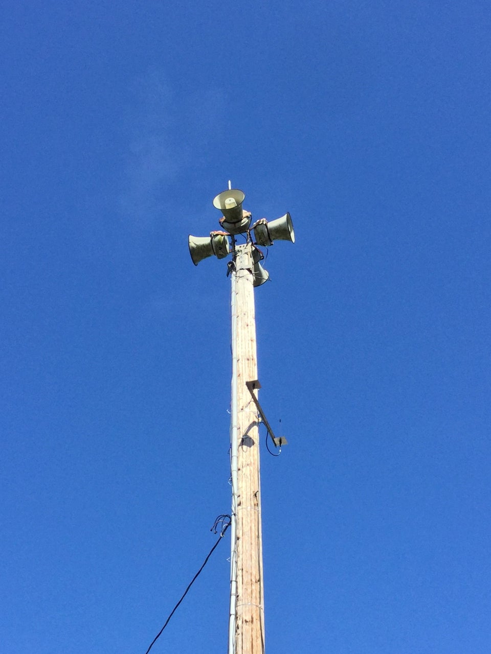 Old air raid sirens on a tower in front of blue skies.