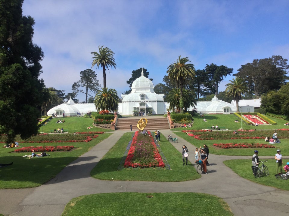 The Conservatory of Flowers buildings with the flower gardens in the foreground under a blue sky with scattered clouds.