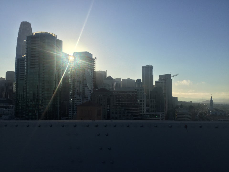 Bay Bridge view of the San Francisco skyline, the setting sun poking through a couple of the buildings with a lens flare