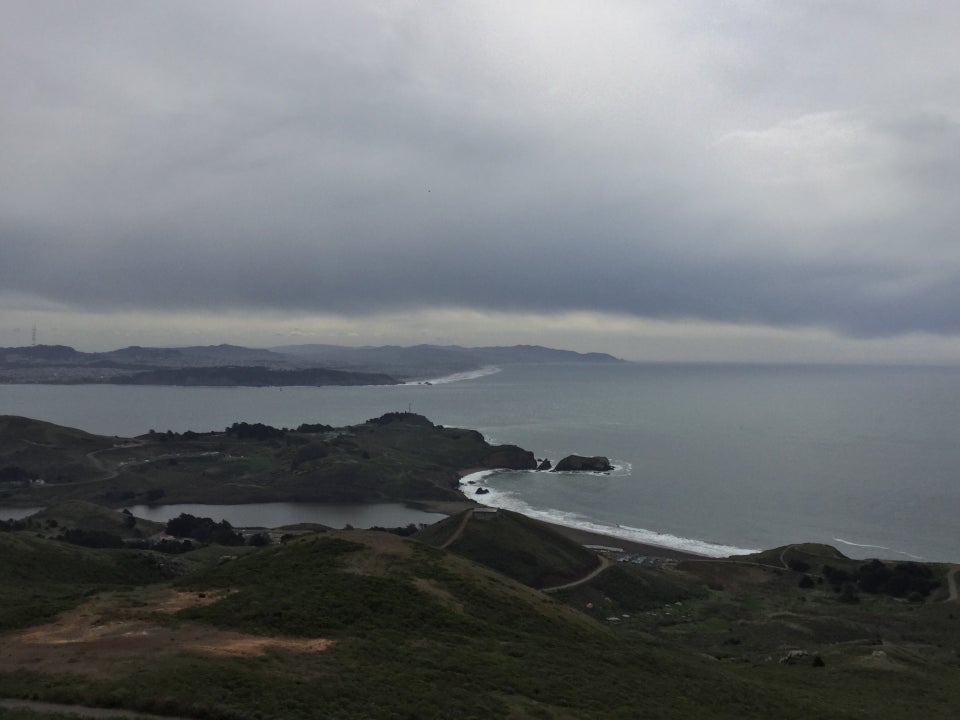 Cloudy skies over the Pacific Ocean, looking down on Rodeo Beach and lagoon, green hills on both sides of them.