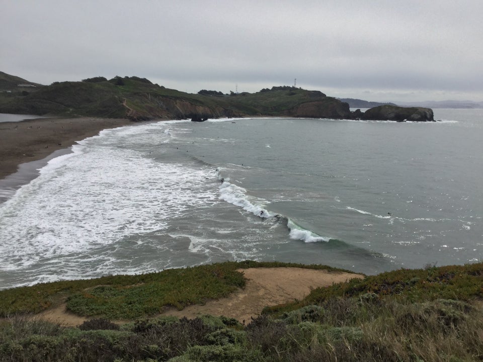 Rodeo Beach with large waves breaking, several surfers catching the waves and surfing.