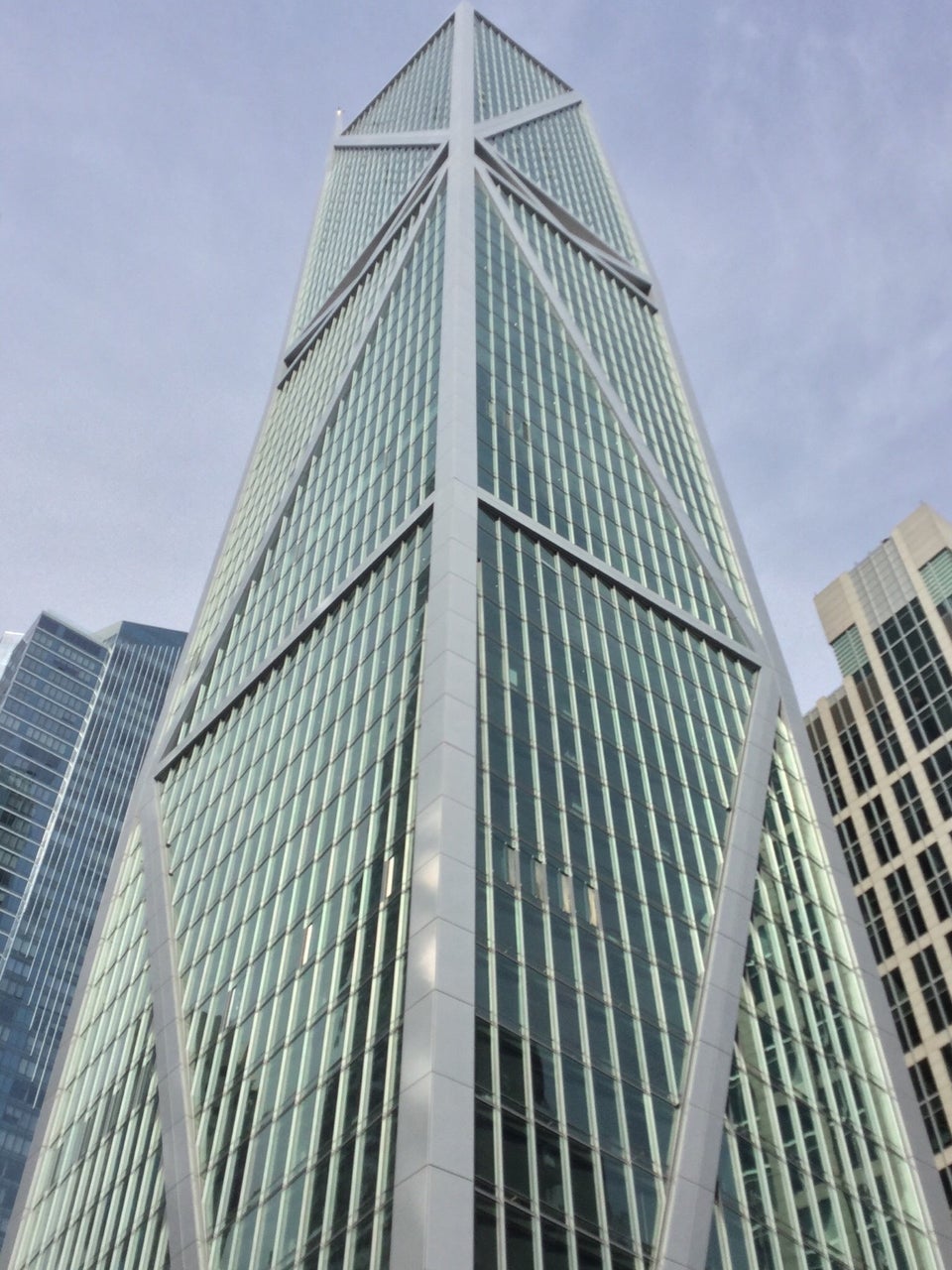 Looking up to the 181 Fremont building, a skyscraper with rectangular segments on its sides each crossed with a single diagonal, alternative so the diagonals look like they connect, with buildings on either side of it partially visible.