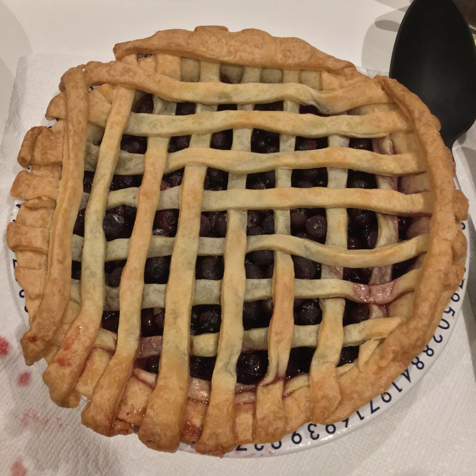 Blueberry pie with the edge of its pi tin showing in the lower right, atop a white table, black serving utensil in the top right.