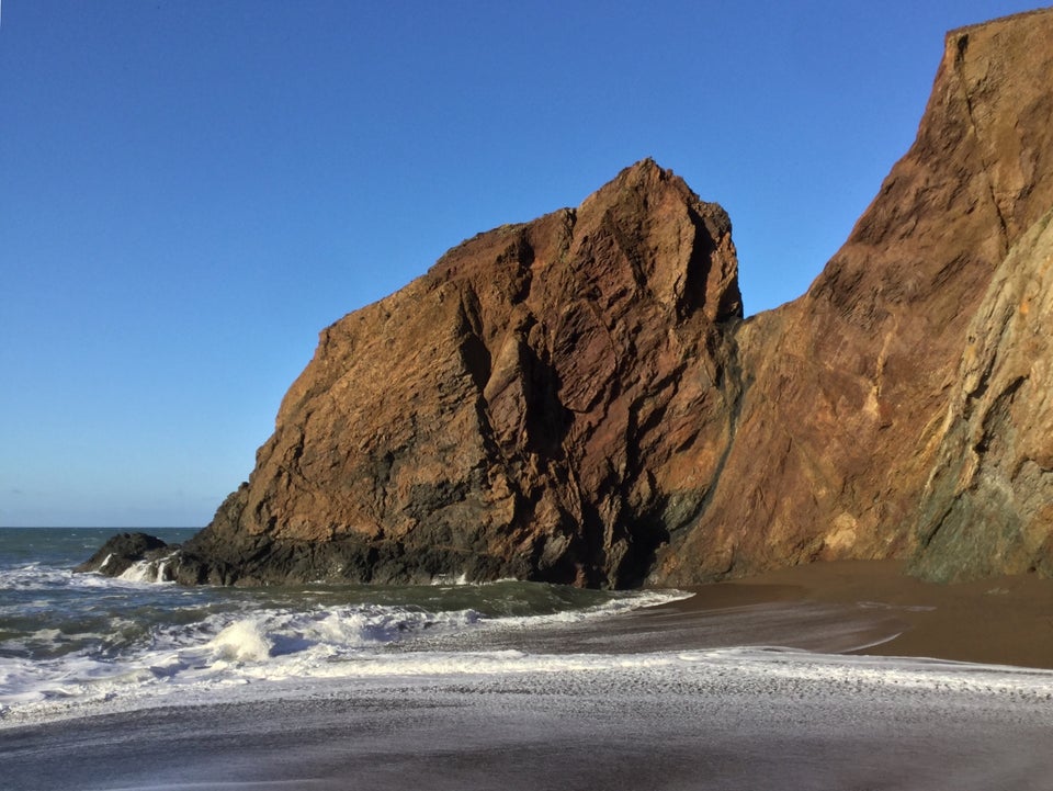 Red rocky outcroppings rising out of the ocean and sand at Tennessee Valley beach