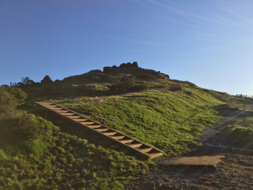 Corona Heights Park, stairs going up and to the left on the green hill with rocky outcroppings on top.