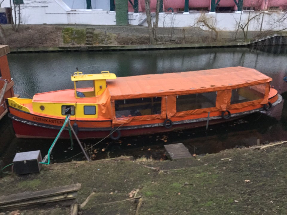 Brightly orange and yellow colored houseboat docked to the shore of a canal.