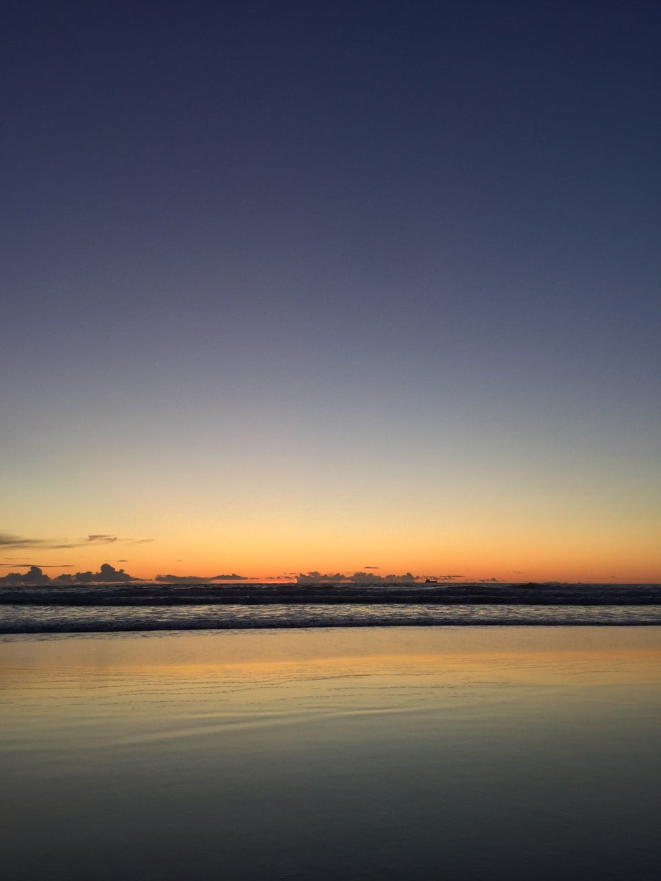 Clear skies just after sunset above waves crashing at Ocean Beach, wet sand reflecting the orange horizon and color gradients in the sky.