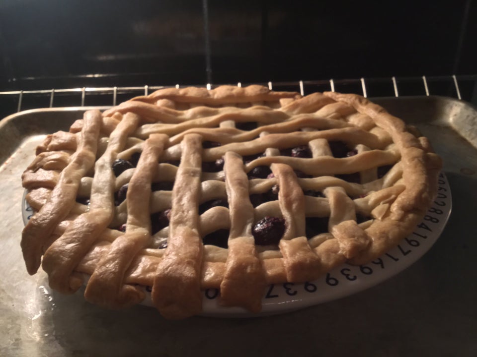 Freshly baked blueberry pie with latticed dough on top, its pie tin sitting atop a metal tray on the lower shelf of an oven.