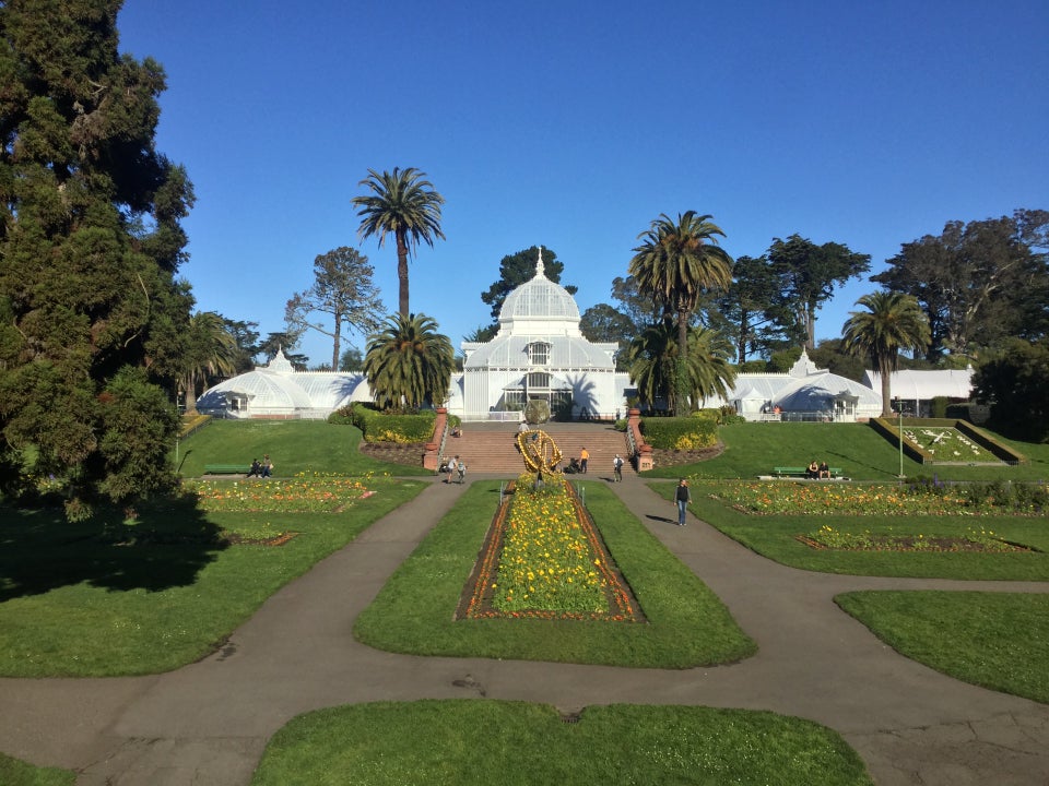 Conservatory of Flowers building in Golden Gate Park under a clear blue sky, with flower beds, lawns, and paths in the foreground.