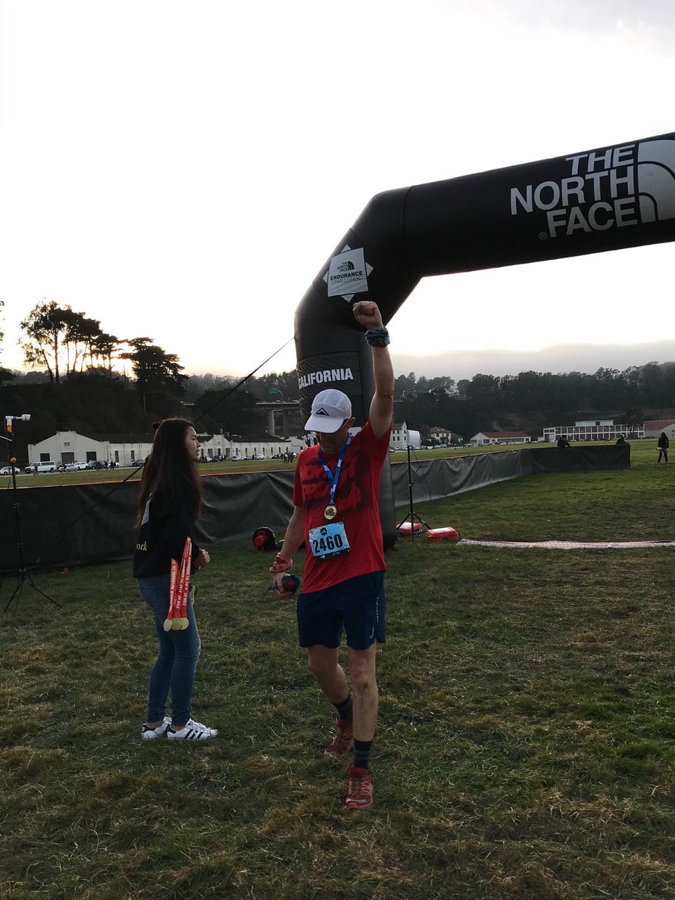 Tantek wearing a 50k finisher’s medal just past the The North Face Endurance Challenge finish line in Crissy Field, San Francisco, bowing his head, raising his left fist to the sky.