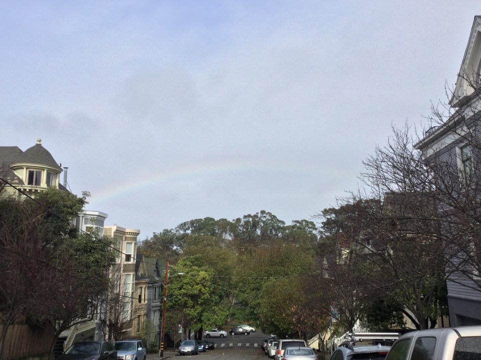 Rainbow in partly cloudy sky looking down Lyon street with houses on both sides.
