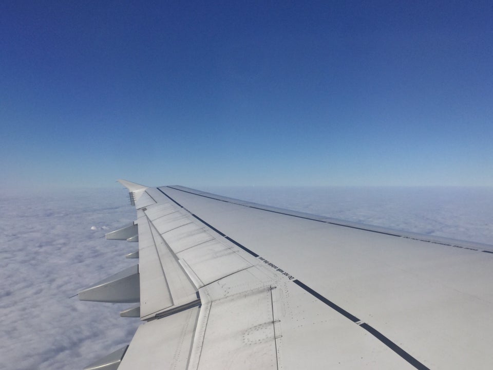 Deep blue sky gradienting to light blue then white above above a blanket of clouds, with an airplane wing extending from the viewer’s perspective.