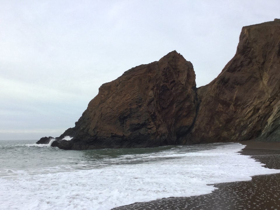 Jagged rocky outcropping extending into the ocean, with surf and a sandy beach in the foreground.