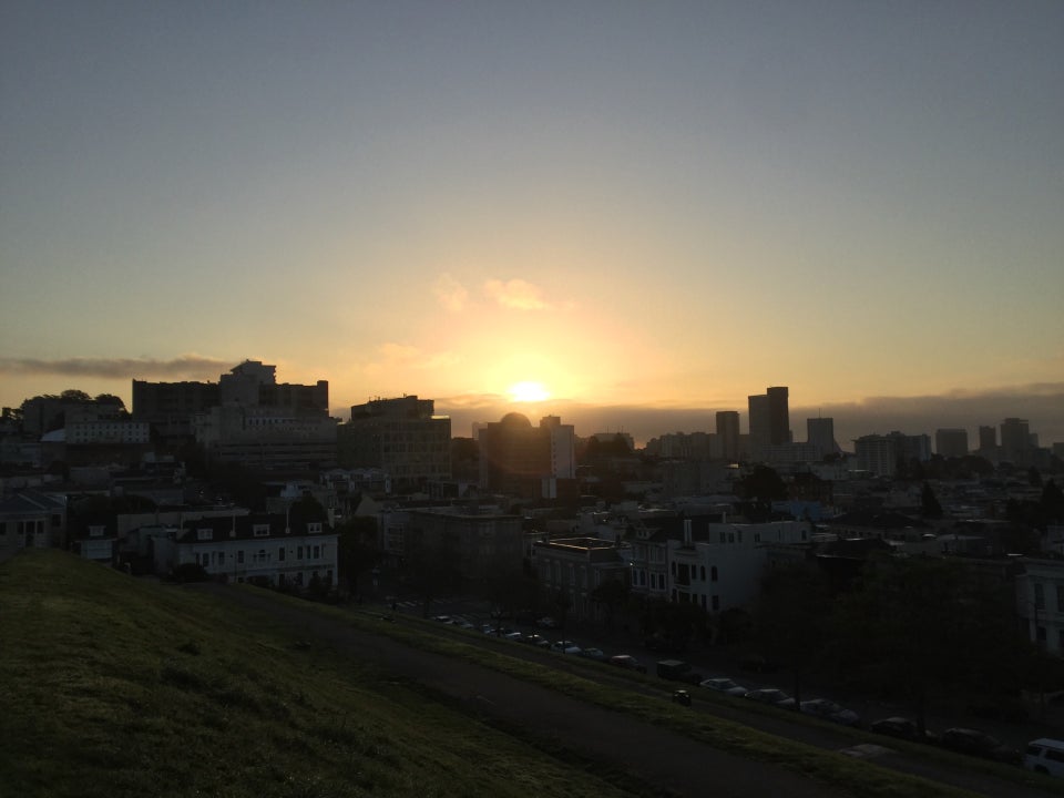 Sunrise just above low clouds backlighting the San Francisco skyline, lighting up the paths and green grass of Alta Plaza Park.