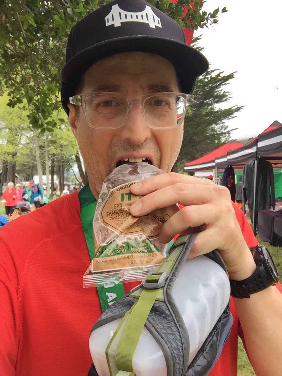 Tantek about to eat an It’s It after finishing the Double Dipsea race, trees, other runners, and race tents behind him