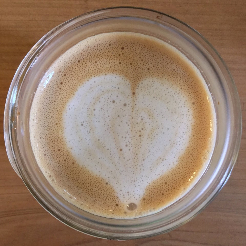 Cream colored heart on a lightly foamed latte in a glass mason jar sitting atop a woodgrain table.