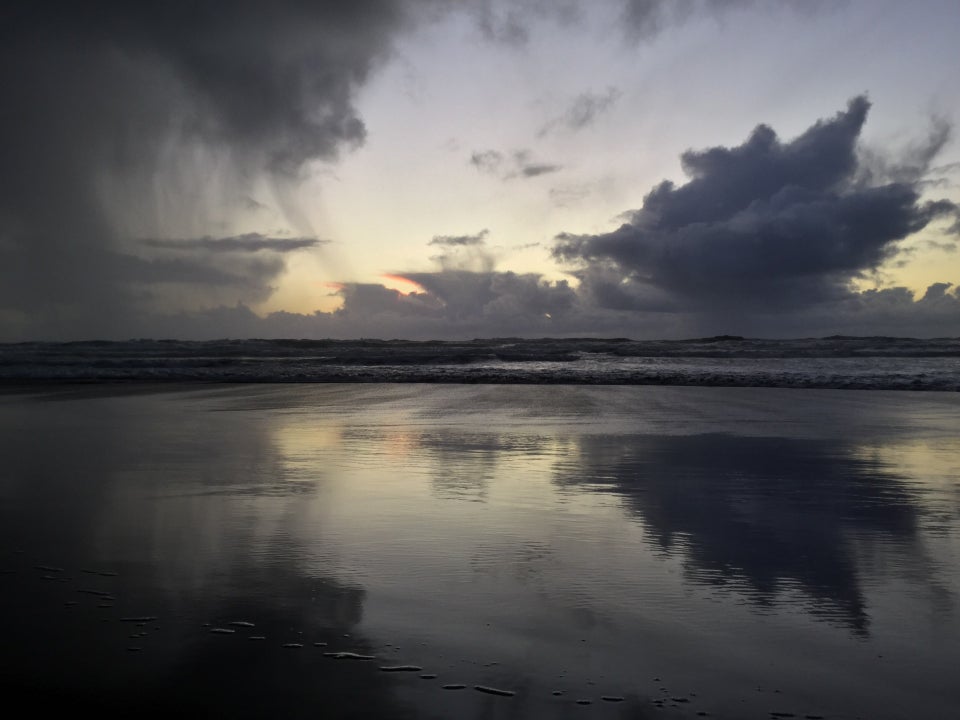 Dramatic storm cloud shedding some rain, distant open twilight sky with clouds lined with an orange tinge from the distant sunset, nearer spiky cloud dark underneath, all reflected by the wet smooth sand in front of Ocean Beach waves.