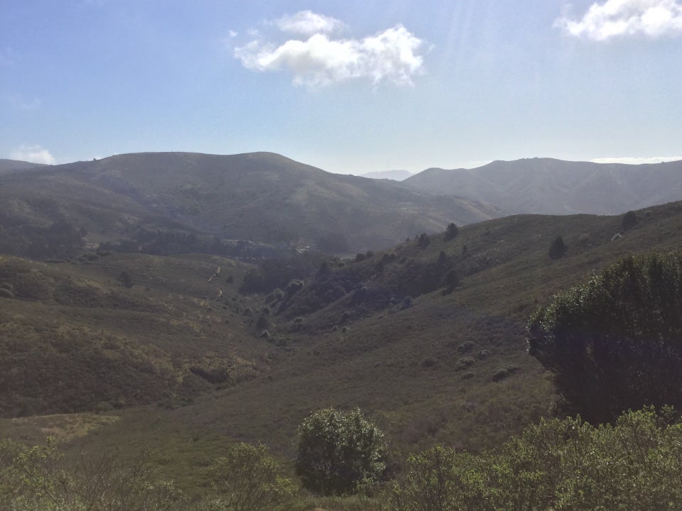 Clear skies with just a couple of puffy clouds above the Marin Headlands, Tennessee Valley in front of them, and a green valley below and in front.