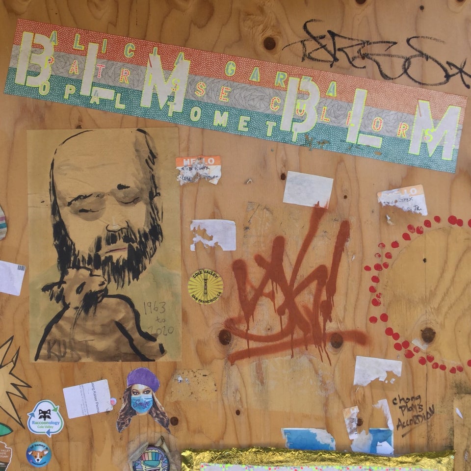 White BLM repeatedly stenciled on multicolor background segment on plywood decorated with additional art.