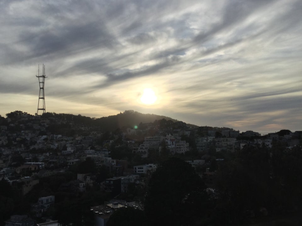 White to dark gray clouds, lit by a setting sun, Sutro Tower reaching skyward from the top of the hills, apartments and houses below in the shade.