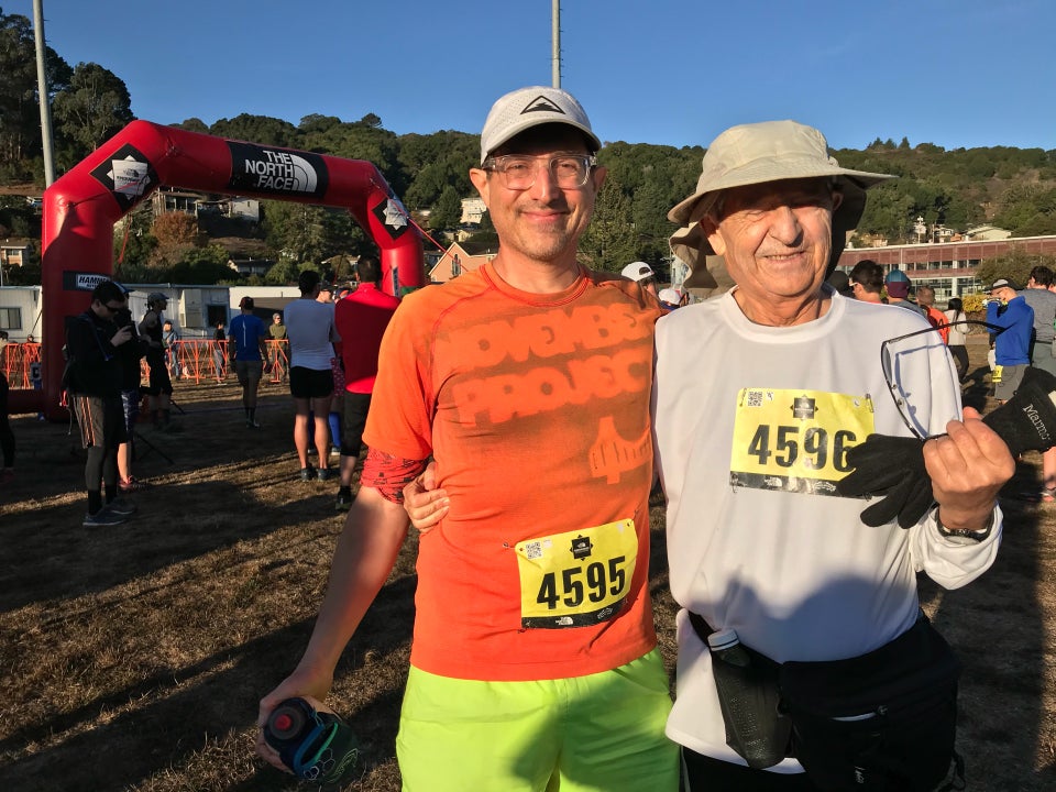 Tantek and Hasan in the morning sun in front of The North Face Endurance Challenge starting arch on a sports field in Marin City, with a forested area in the distance under a clear blue sky.