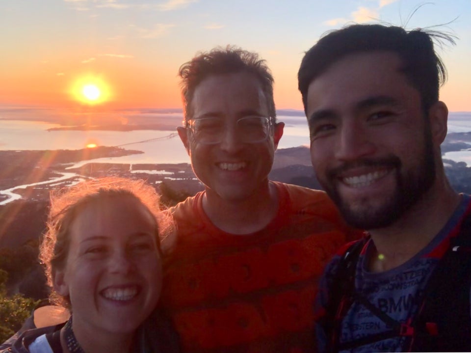 Kat, Tantek, and Bryan at the top of Mt. Tam with the sun rising just about the bay in the background, sun beams and an orange glow backlighting their hair and faces.