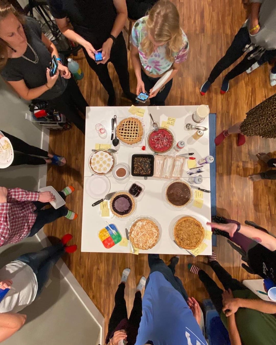 Bakers and friends standing around a table of pies, taking photographs.