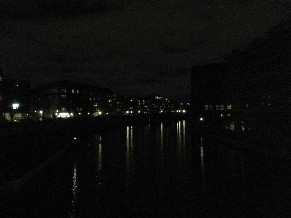 Buildings with only a few lights across the photo, reflections of the lights drawn out in the dark canal below, viewed from a bridge.