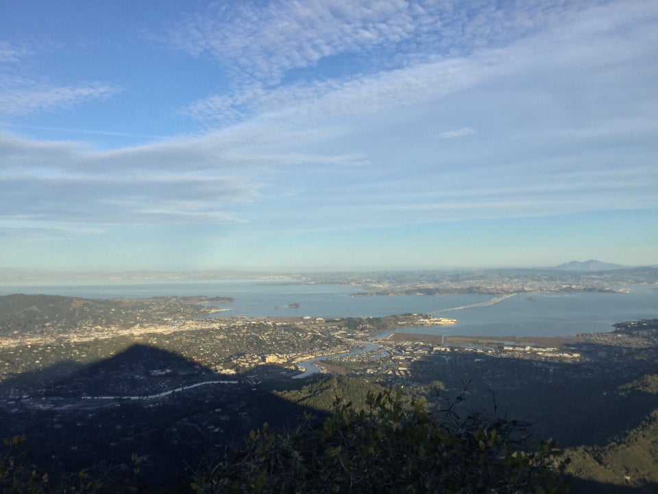 Partly cloudy sky above a view of the East Bay, Richmond Bridgy, the bay itself, and Mount Tamalpais shadow starting to cover the land below.