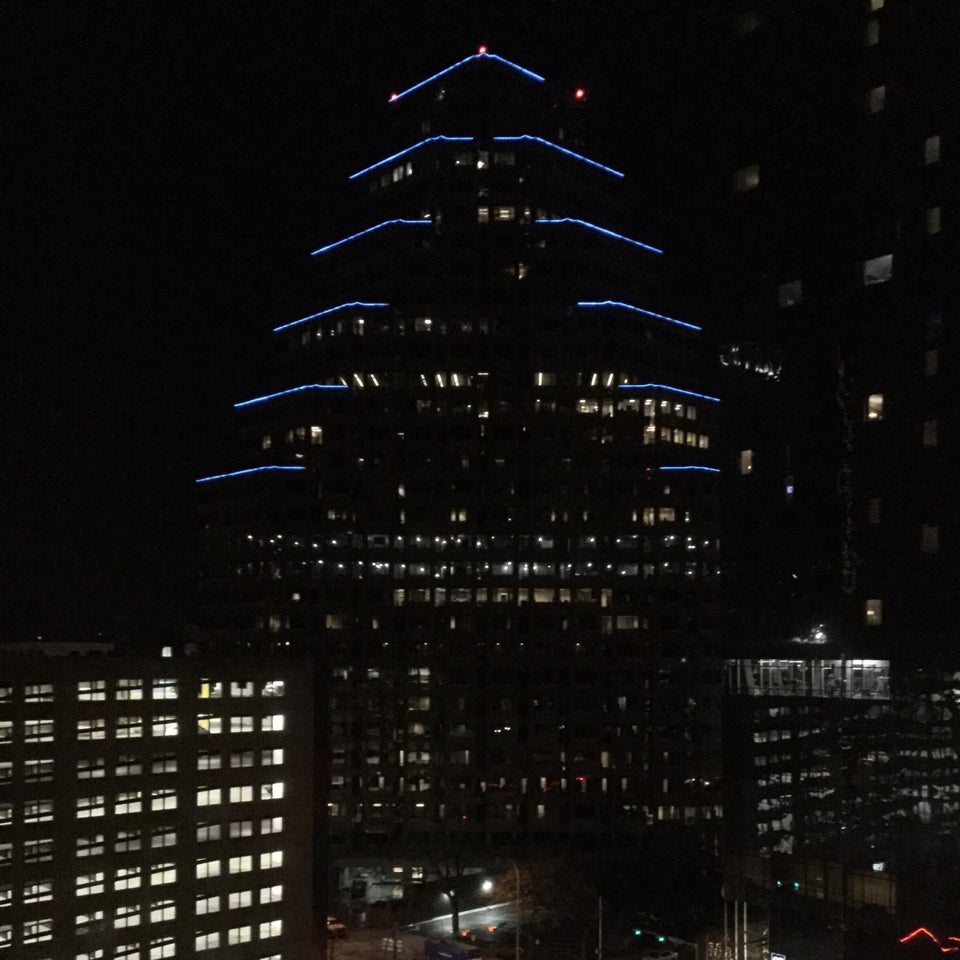 Building with pyramid shaped terraces at night, with blue lights glowing on each of the terrace corners. a few more downtown Austin buildings at night.