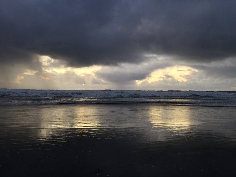 Dark storm clouds with just a few gaps behind them where the light sky shined down, showing a reflecting on wet sand in front the waves at Ocean Beach.