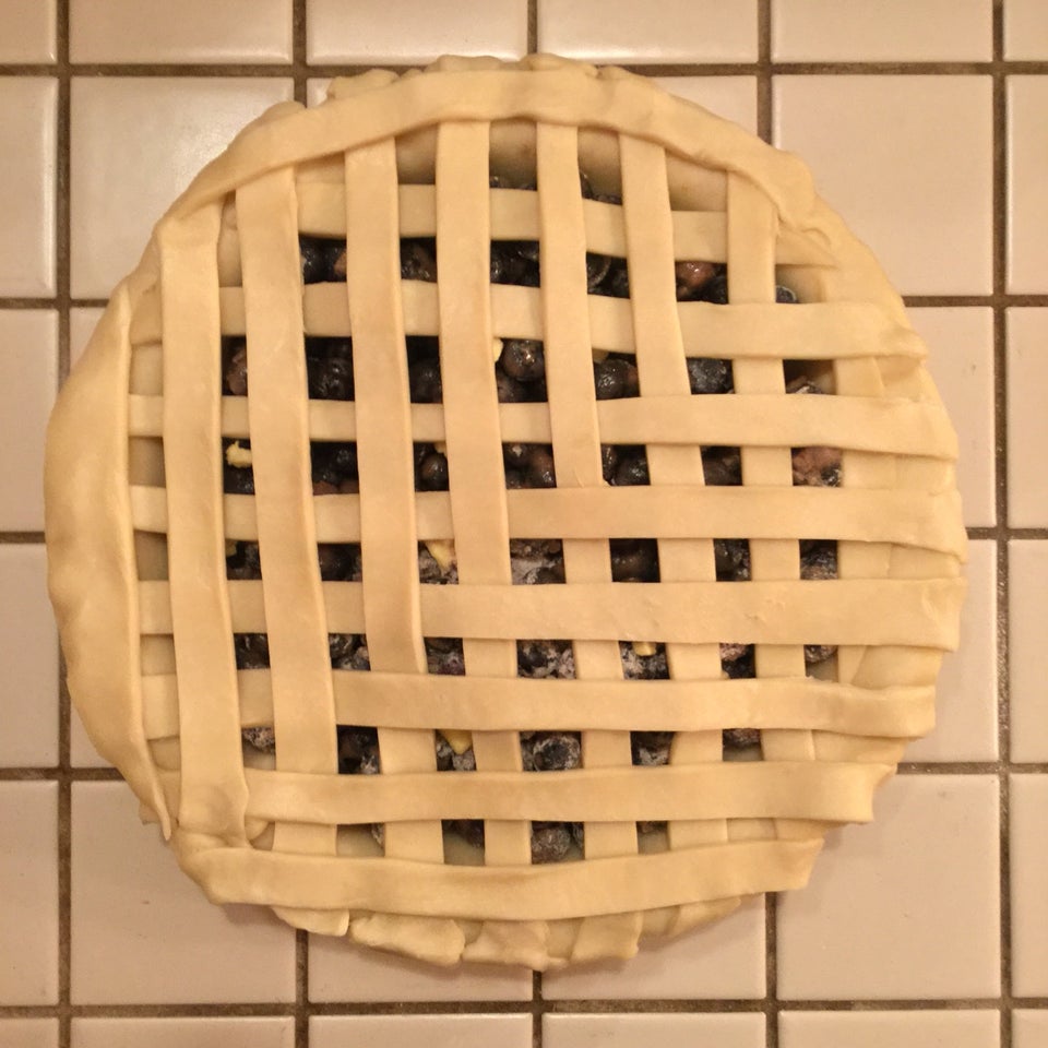 Blueberry pie made, with a latticework top, atop an off-white tile countertop.